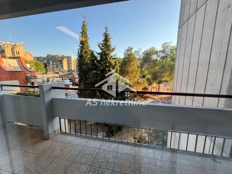 Pogled sa popločane terase na drveće i okolne zgrade.