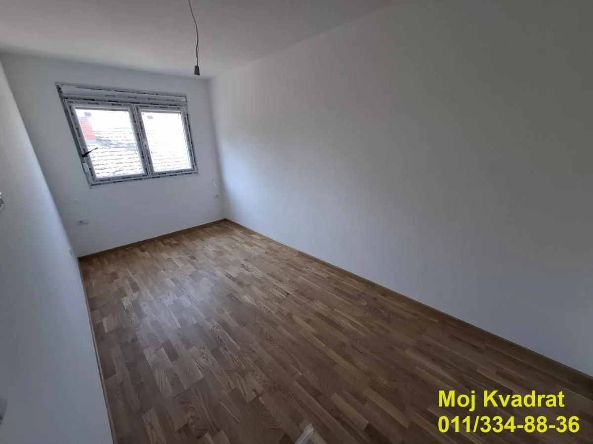 Prazna soba sa parketom i belim zidovima.