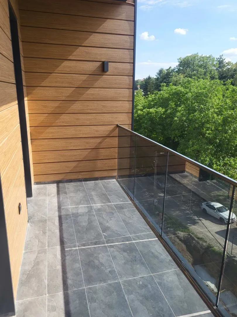 Moderan i prostran balkon obložen pločicama sa staklenom ogradom.