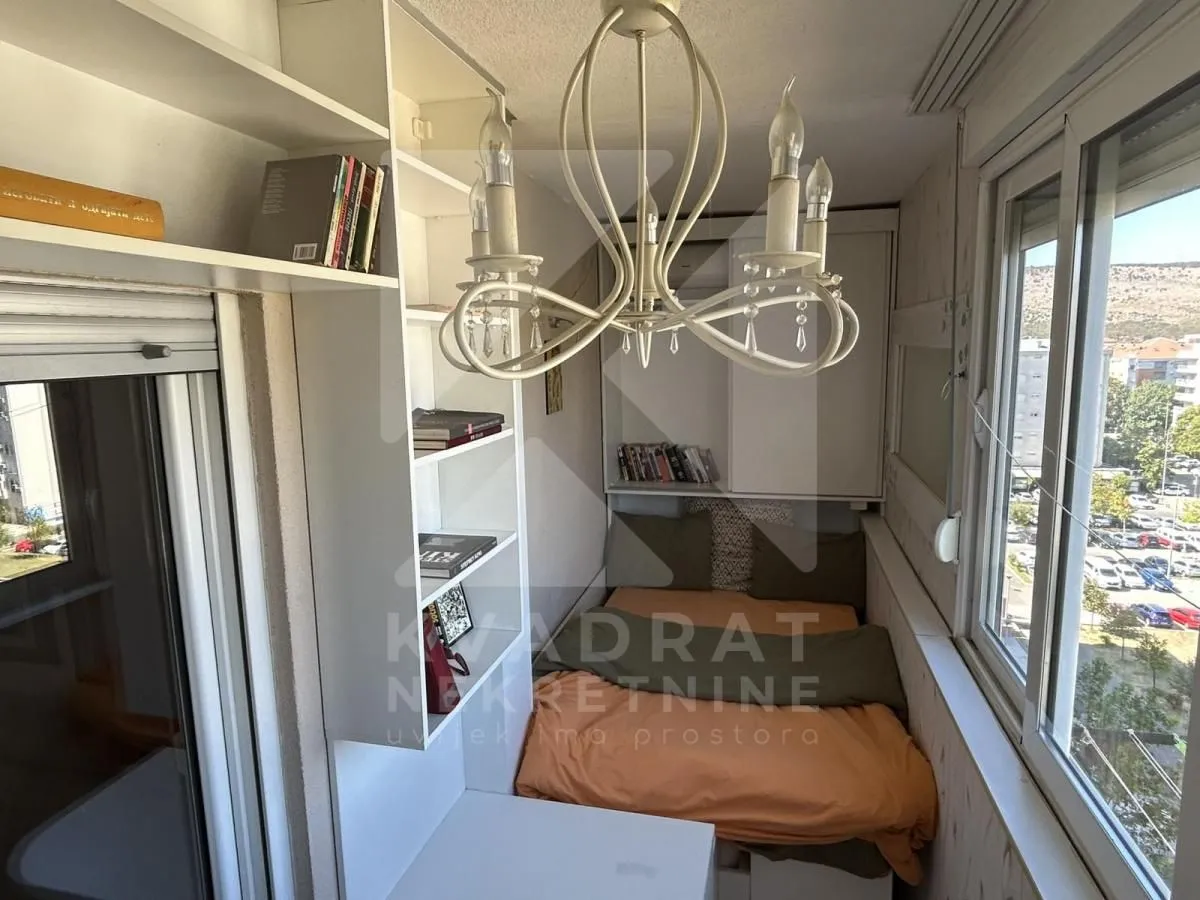 Smaller bedroom with a bed, bookshelves, and a chandelier.