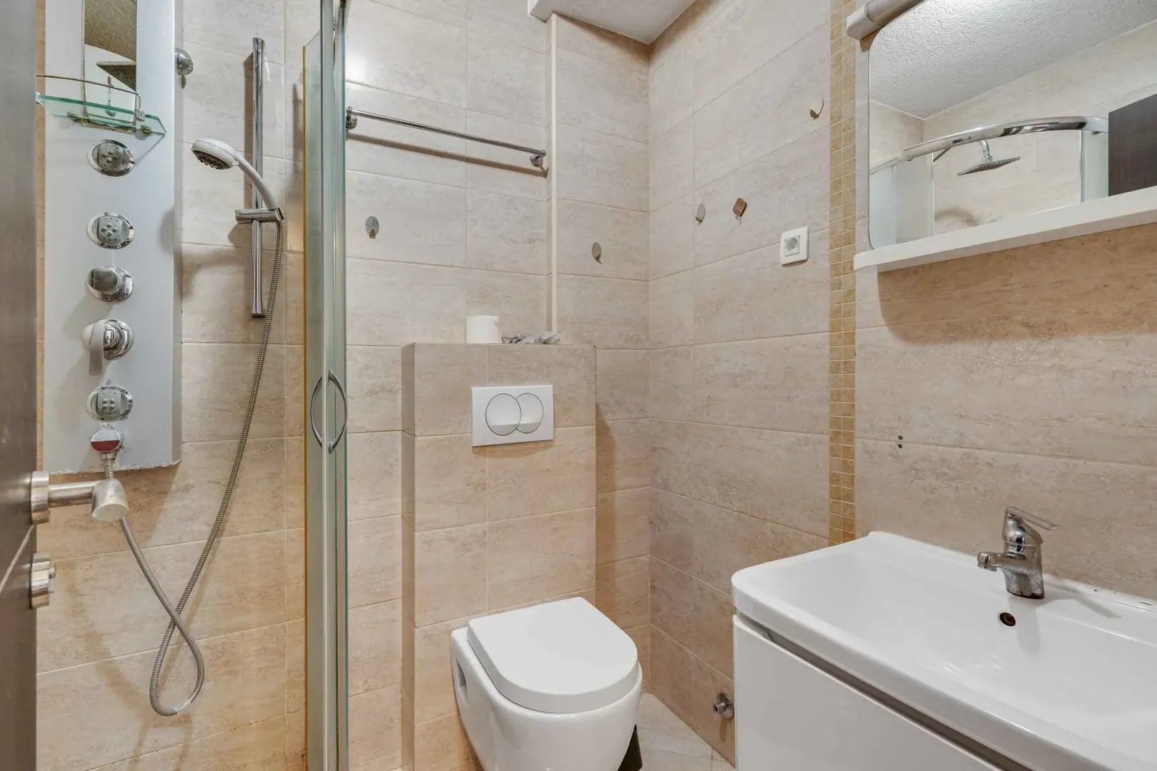 Manje kupatilo sa tuš kabinom, umivaonikom i WC šoljom u bež tonovima.