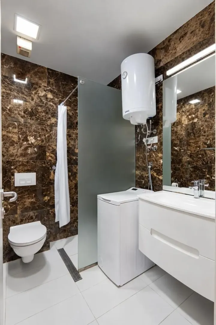 Modern bathroom with a walk-in shower, washbasin, and washing machine.