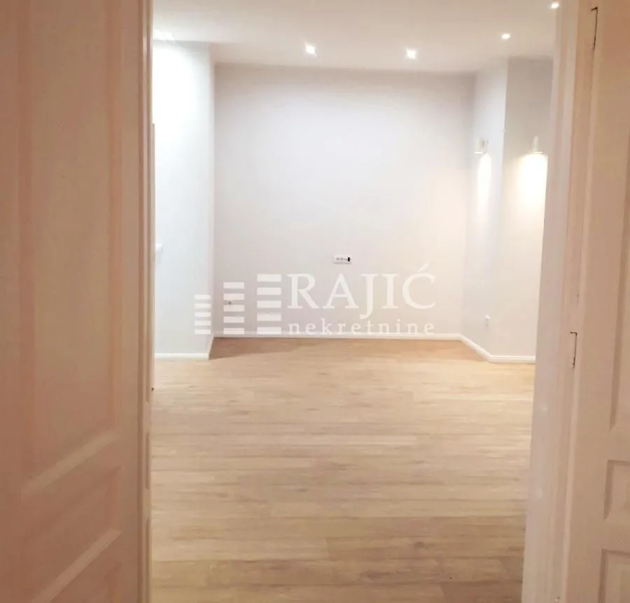 Empty room with laminate flooring and recessed lighting viewed through a doorway.
