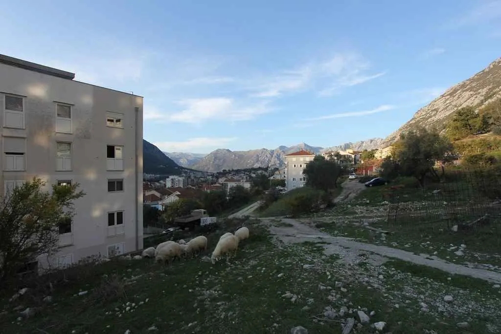 Pogled na stambenu zgradu i okolni pejzaž sa planinama u pozadini.
