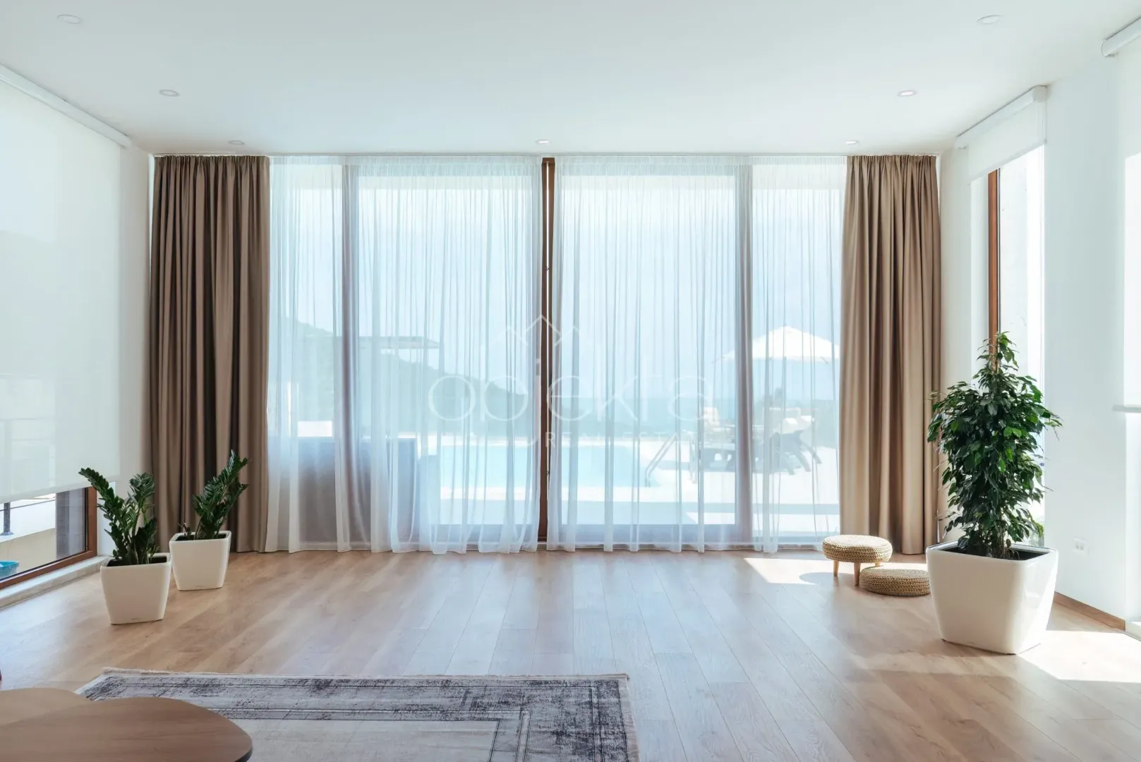 Spacious bright living room with large glass surfaces and a view of the terrace with a swimming pool.