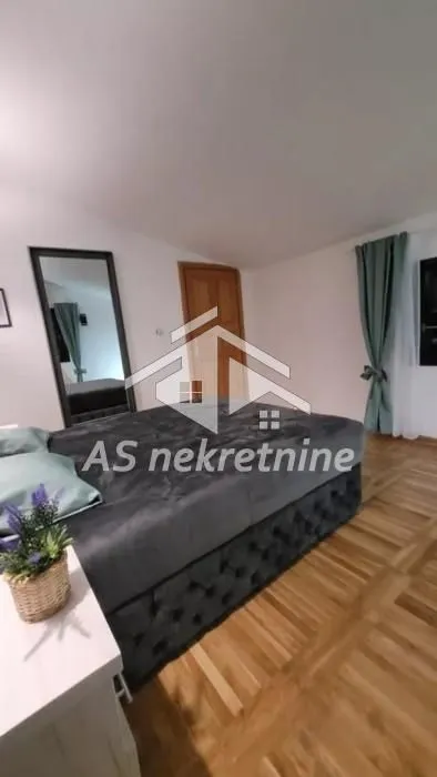 Prostrana spavaća soba sa bračnim krevetom i parketom na podu.