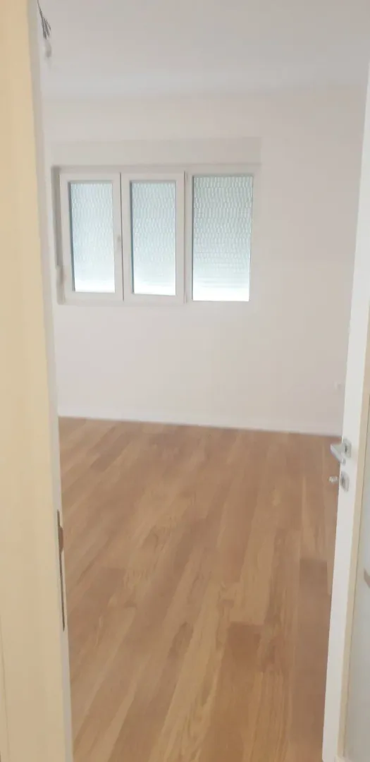 An empty room with light parquet flooring and white walls.