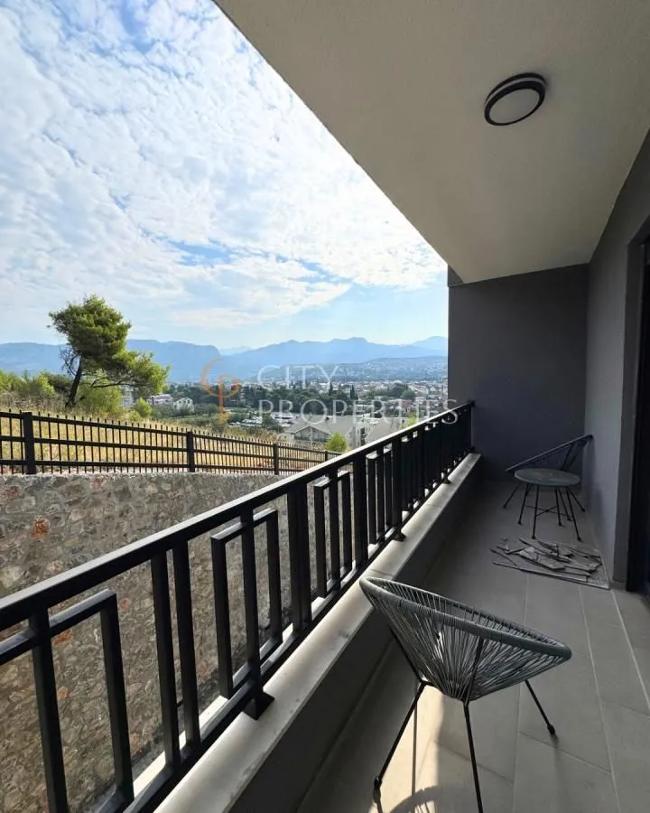 Nakatkriveni balkon sa metalnom ogradom i pogledom na prirodu i grad.