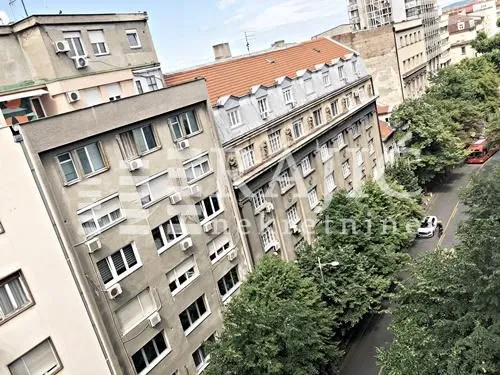 Window view of surrounding buildings and a tree-lined street.
