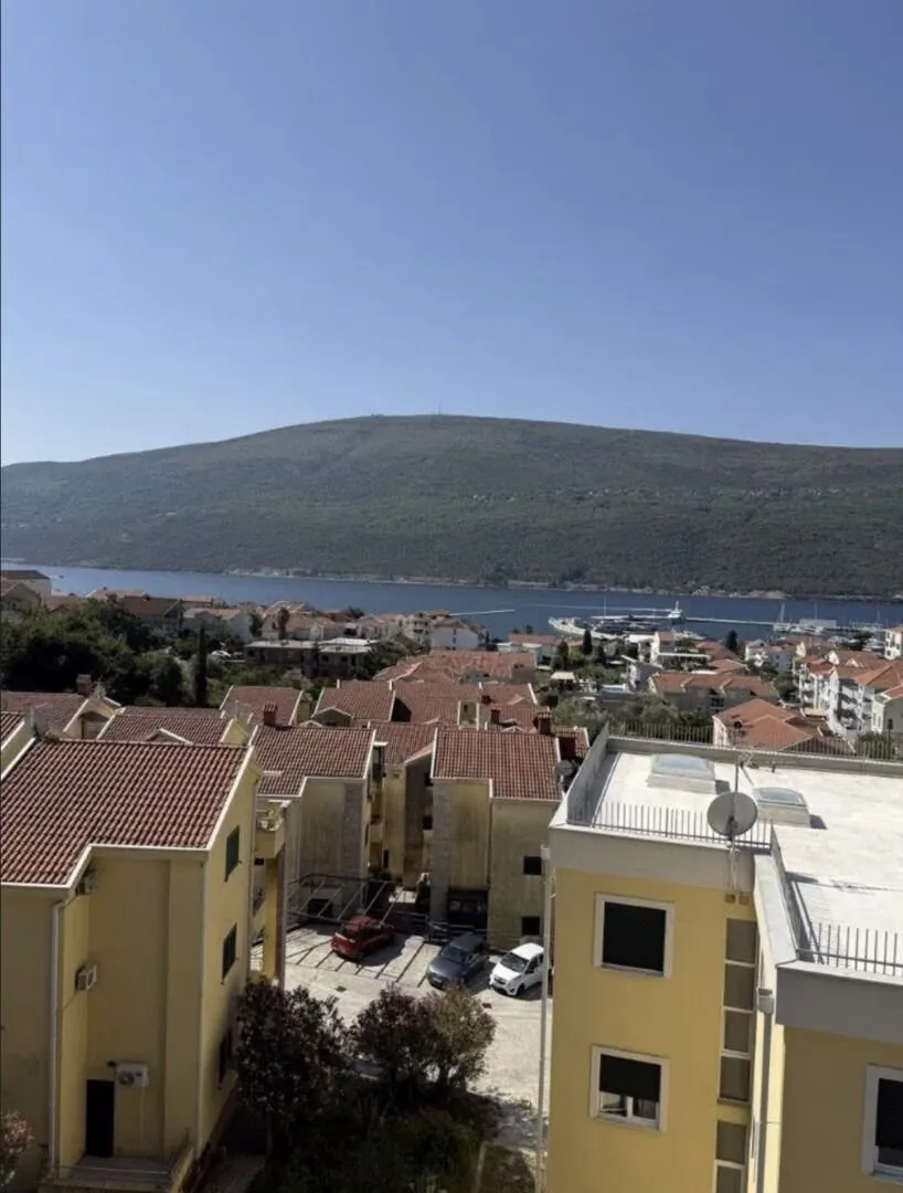 Pogled sa prozora na okolne zgrade, more i planinu.