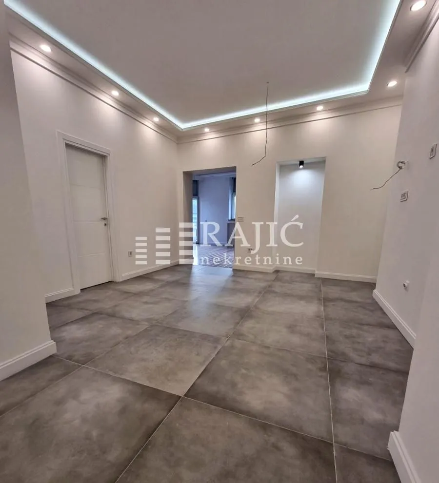An empty room with ceramic floor tiles and a dropped ceiling with lighting.