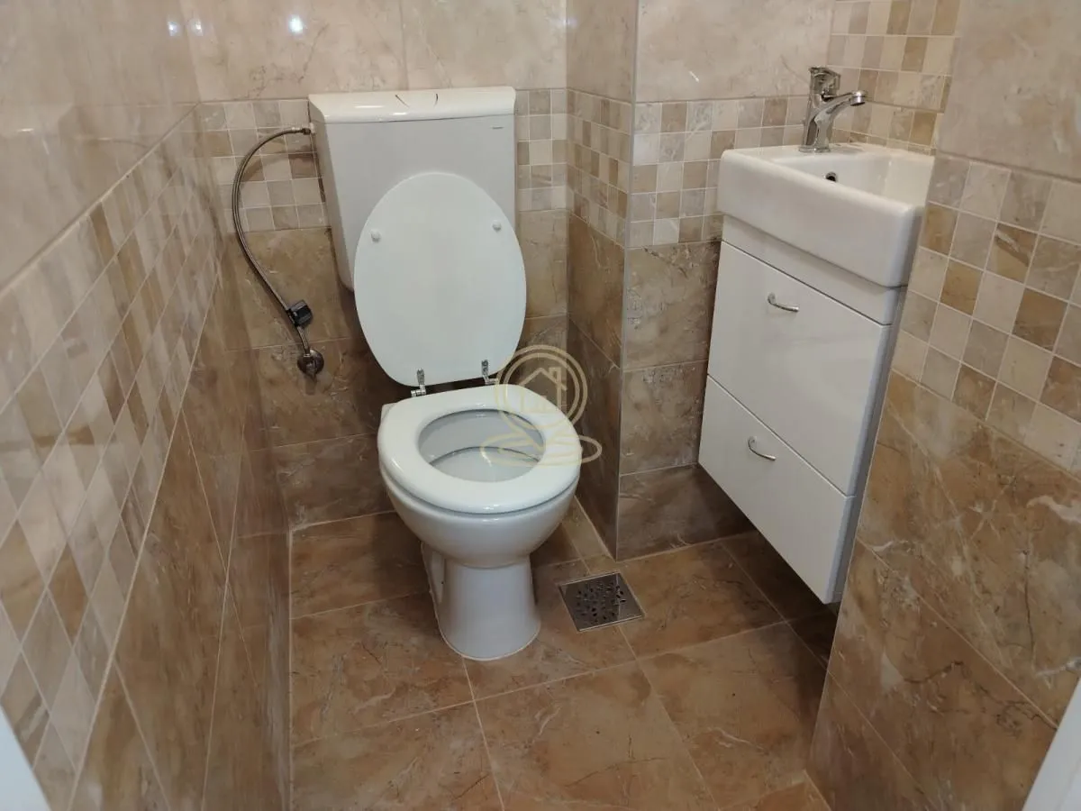 Manje kupatilo obloženo keramičkim pločicama sa WC šoljom i umivaonikom.