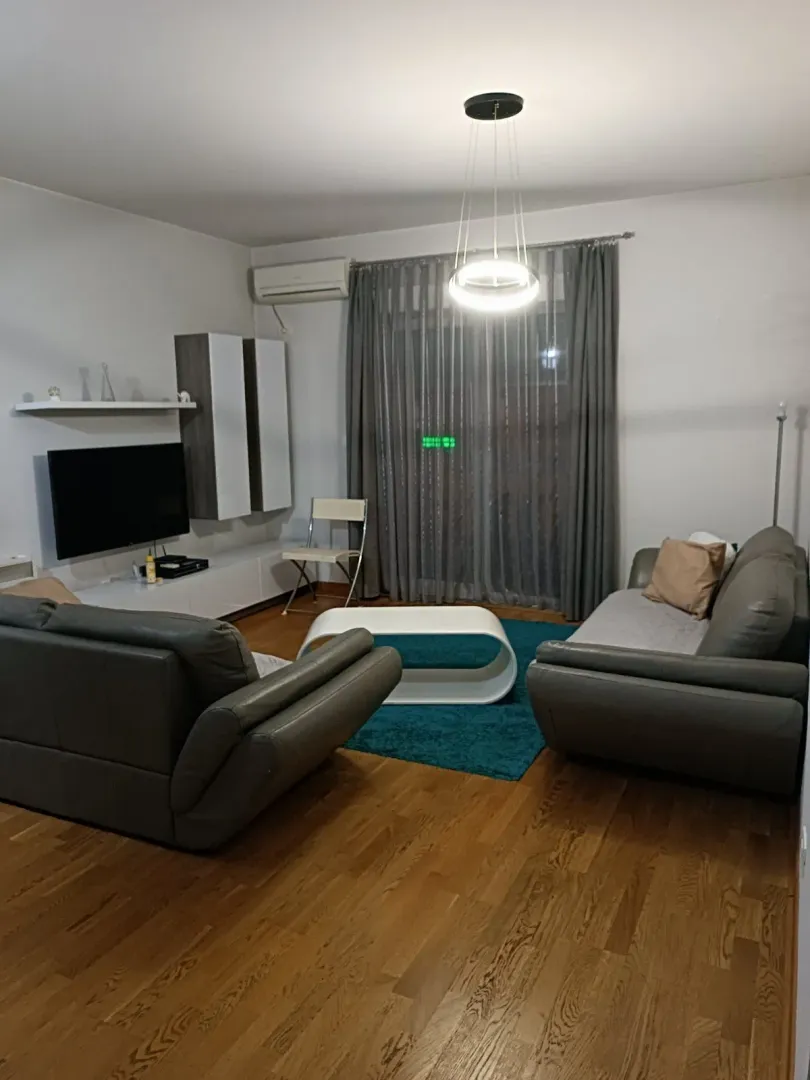 Svijetla dnevna soba sa sivom kožnom garniturom i modernom rasvjetom.