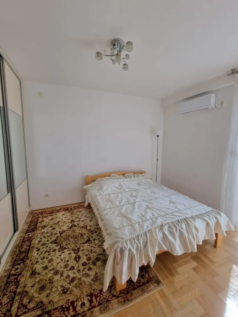 Svijetla spavaća soba sa bračnim krevetom, tepihom i klima uređajem.