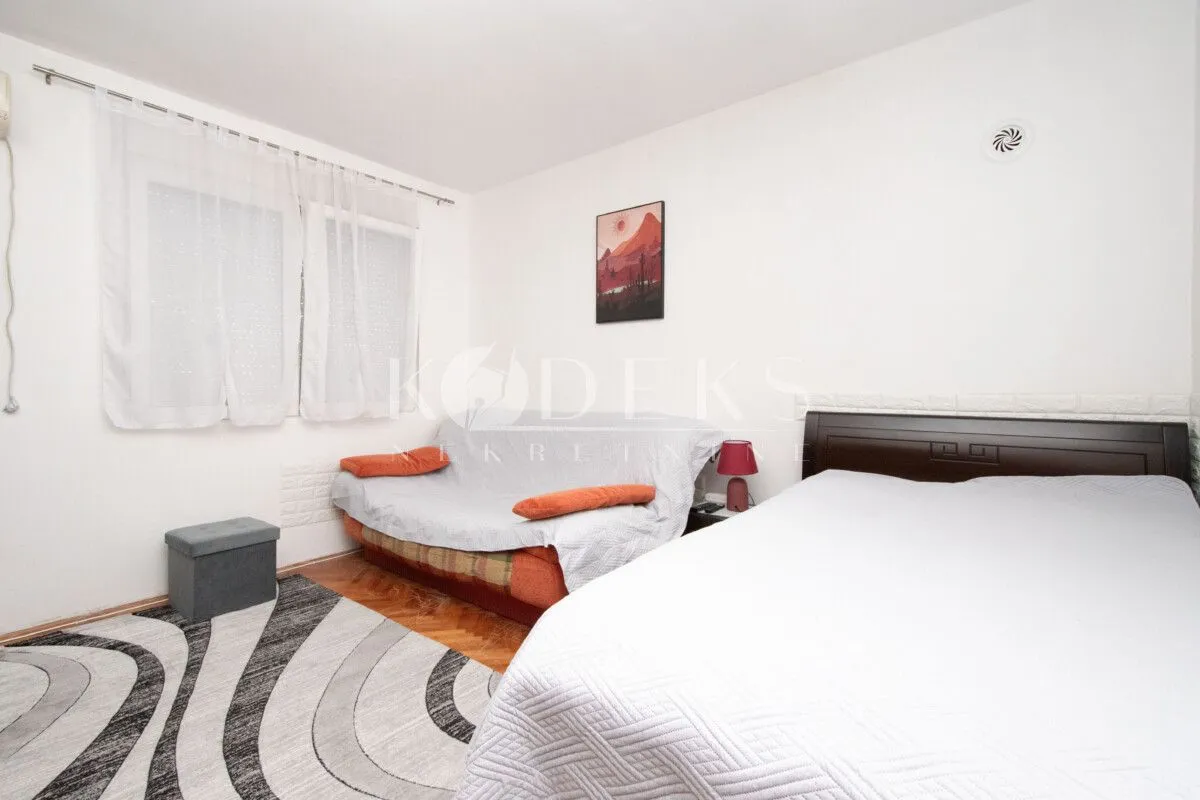 Bedroom with a double bed, a sofa, and a window with white curtains.