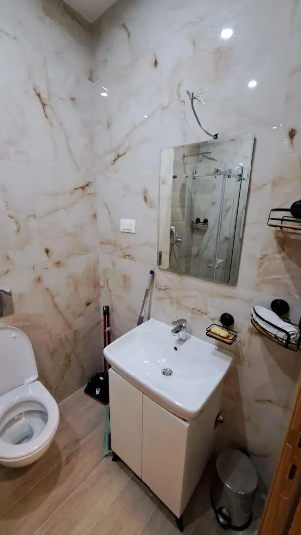 Moderno kupatilo sa svijetlim mermernim pločicama i lavaboom sa ormarićem.