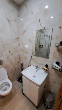 Moderno kupatilo sa svijetlim mermernim pločicama i lavaboom sa ormarićem. - image 6