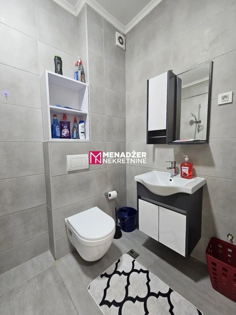 Small bathroom covered with grey tiles featuring a sink and a toilet.