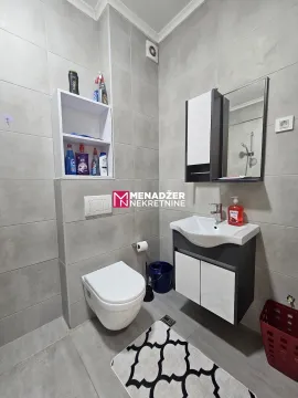 Small bathroom covered with grey tiles featuring a sink and a toilet. - image 4