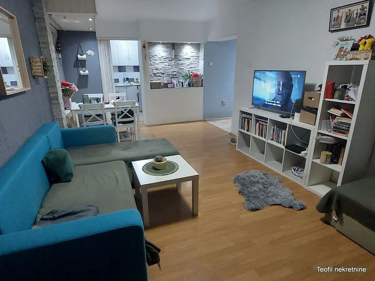 Dnevna soba sa garniturom, TV-om i trpezarijom u pozadini.