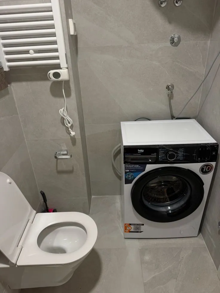 Moderno opremljeno kupatilo sa veš mašinom i sanitarijama.