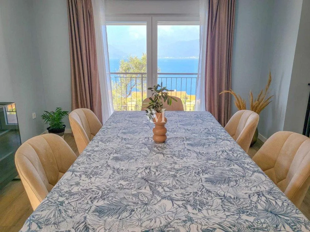 Dining area with a table, chairs, and a sea view through the balcony doors.