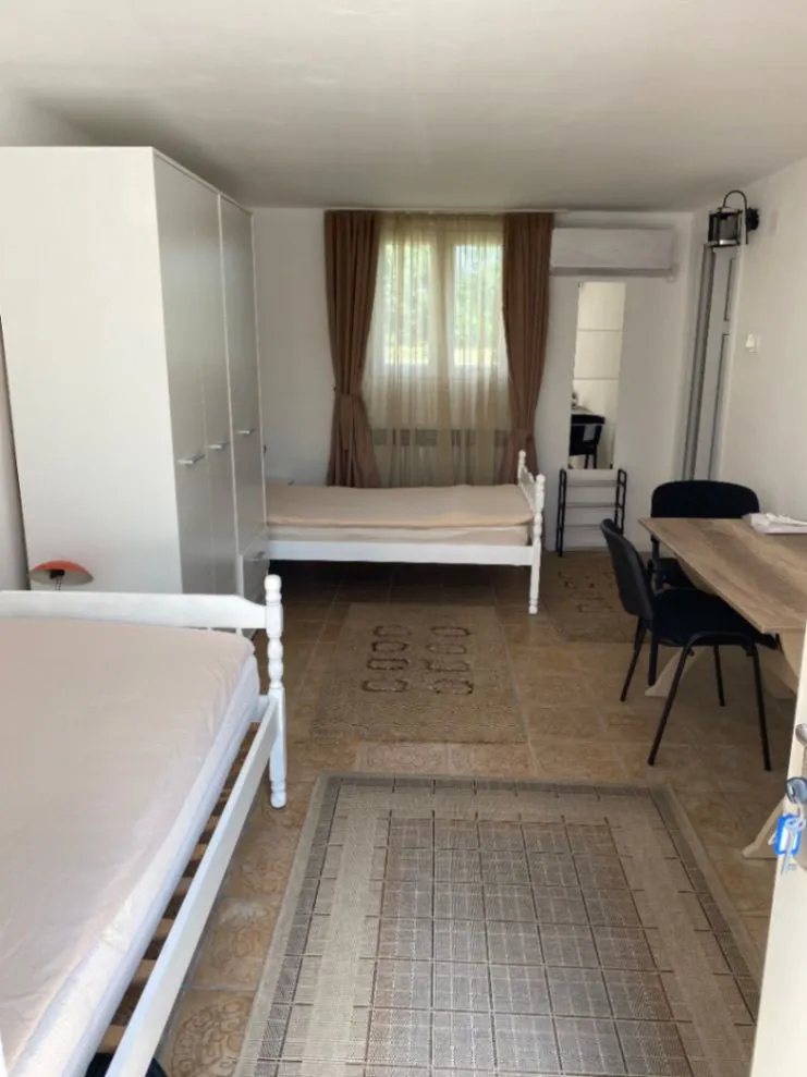 Namještena spavaća soba sa dva kreveta, ormarom i stolom sa stolicama.