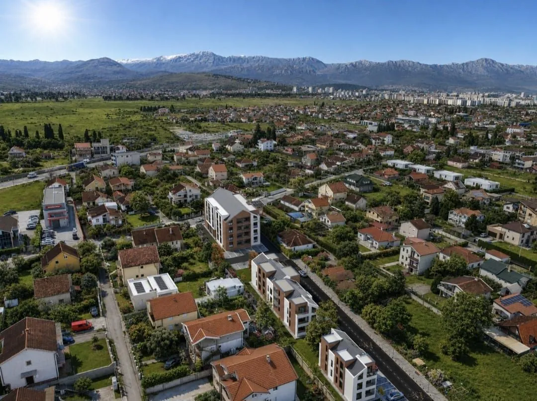 Pogled iz vazduha na gradsko naselje sa zgradama i planinama u pozadini.