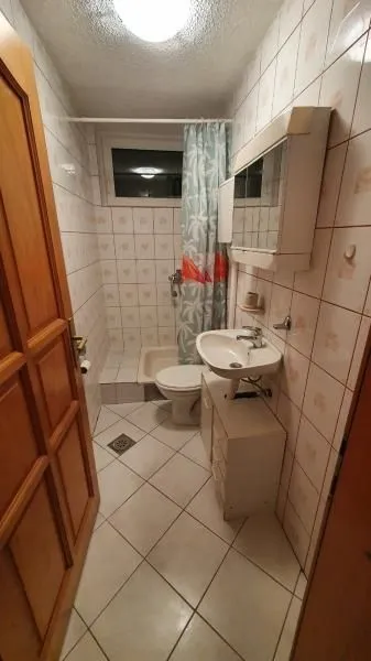 Manje kupatilo sa umivaonikom, toaletom i tuš kabinom sa zavesom.