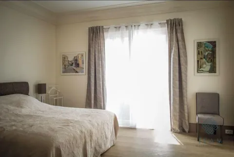 Spavaća soba sa bračnim krevetom, prozorom sa zavesama i umetničkim slikama na zidu. - image 5