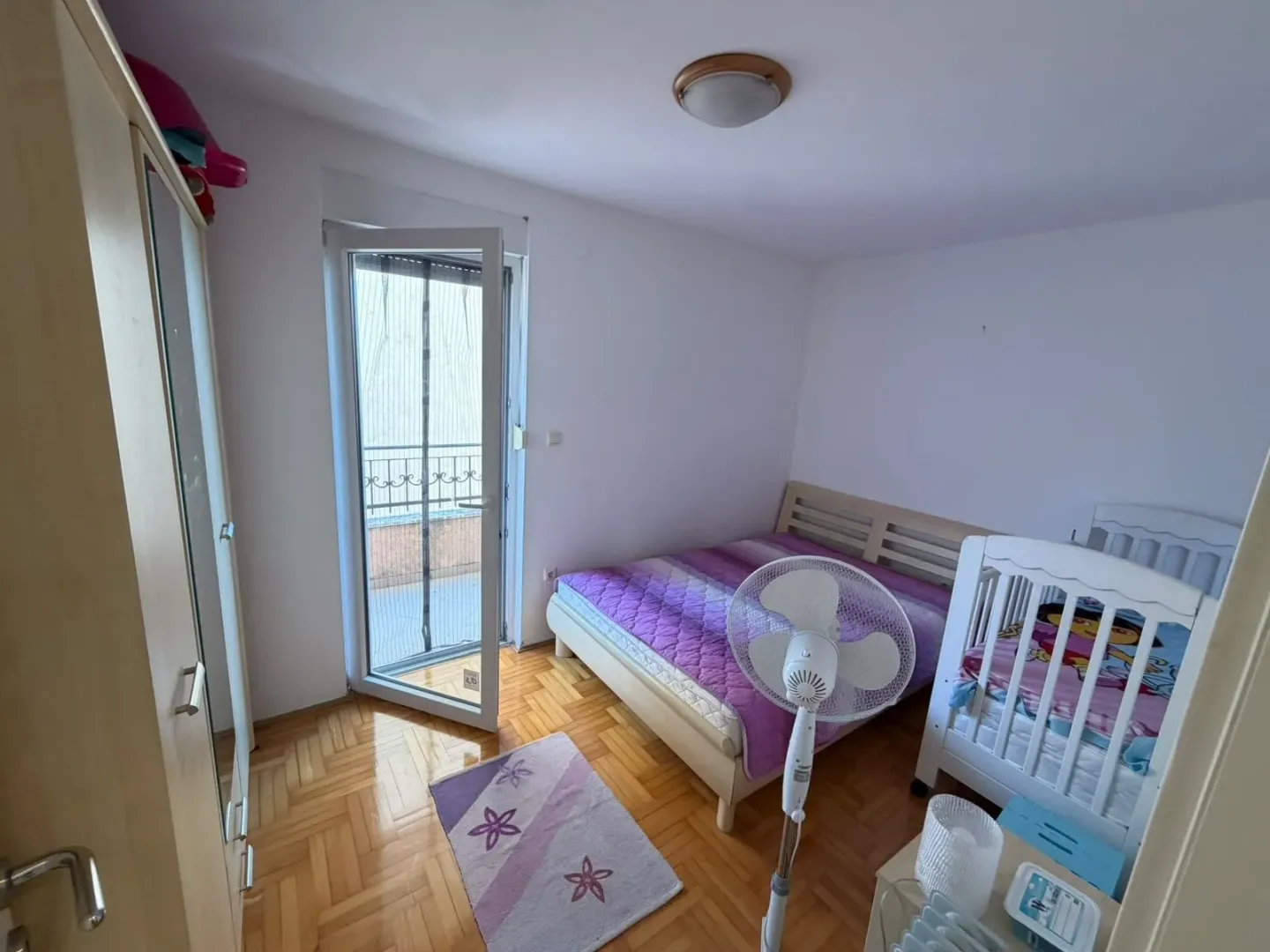 Spavaća soba sa bračnim krevetom, krevetcem za bebe, ormarom i izlazom na terasu.