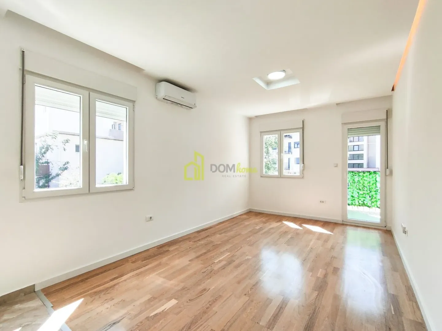 Empty bright room with wooden flooring, air conditioning unit, and windows.