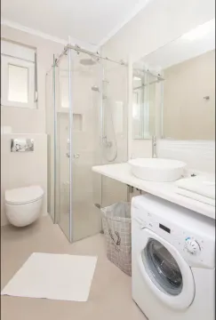 Modernly equipped bathroom with a walk-in shower, basin, and washing machine. - image 11