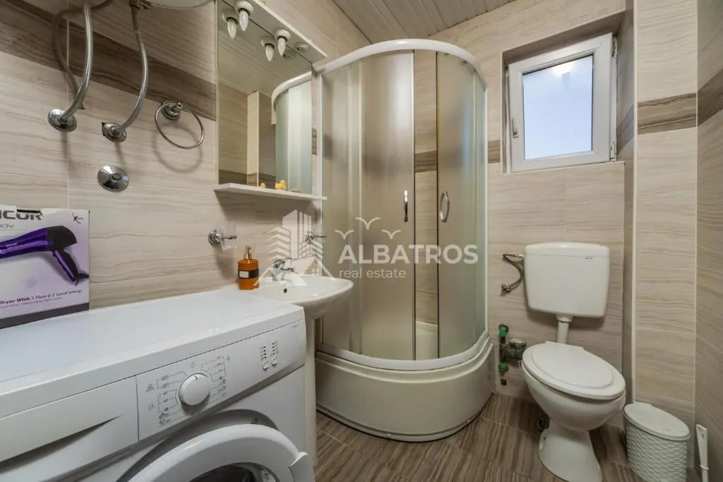 Small bathroom with a shower cabin, washbasin, toilet, and washing machine.