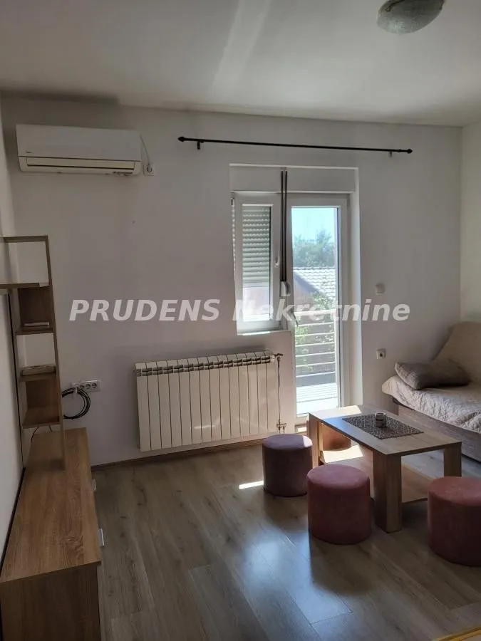 Dnevna soba sa garniturom, stočićem, klima-uređajem i izlazom na balkon.