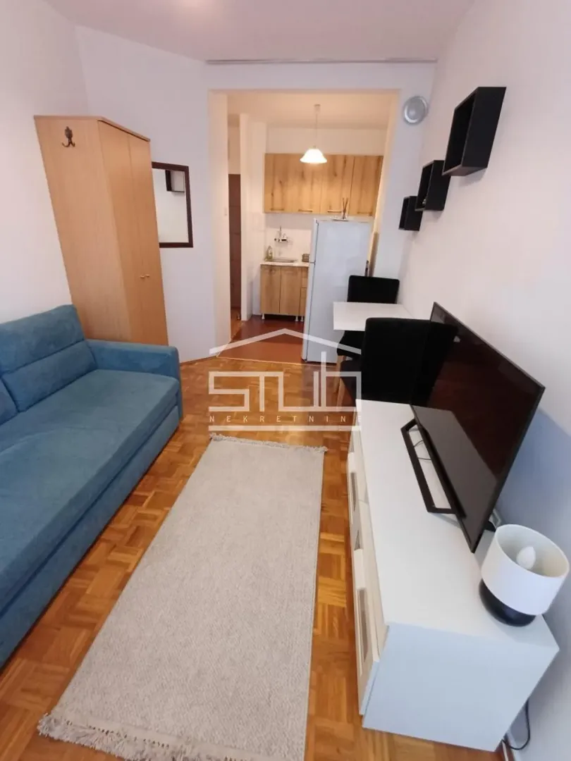 Small living room with a blue sofa, TV unit, and a view of the kitchen.