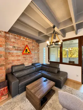 Living room with a leather sectional sofa, brick wall, and wooden coffee table. - image 3