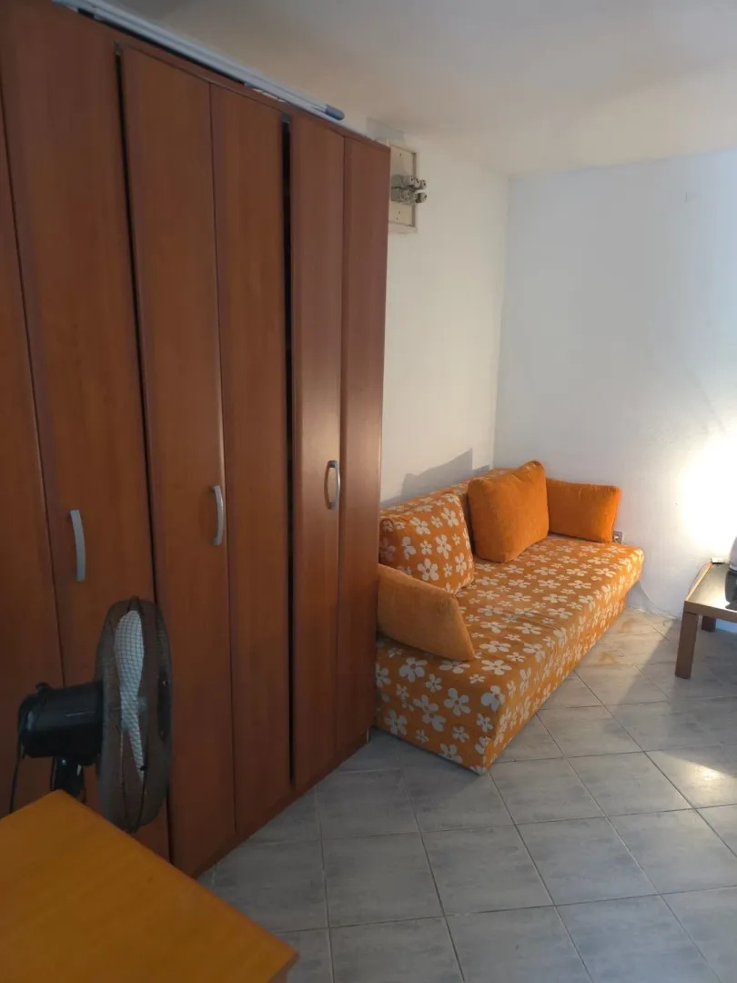 Dnevna soba sa garniturom na rasklapanje, garderoberom i keramičkim pločicama na podu.