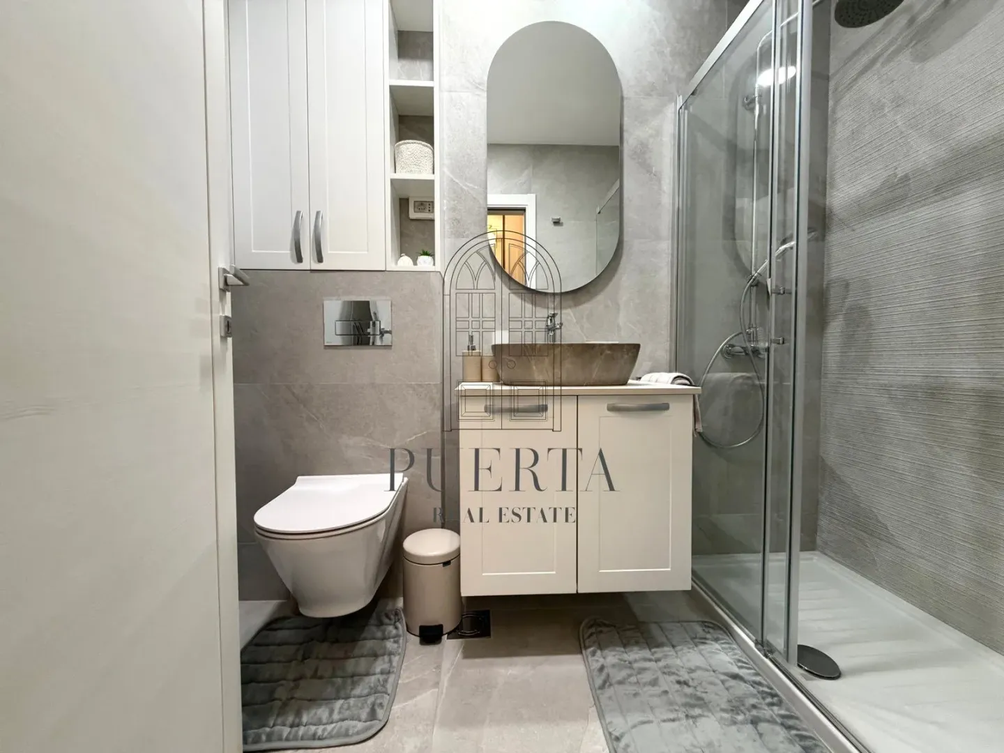Modernly equipped bathroom with a walk-in shower and grey tiles.
