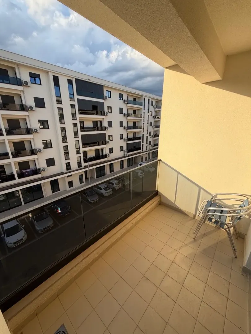 Small balcony with glass railing and chairs, overlooking the neighbouring building and parking lot.