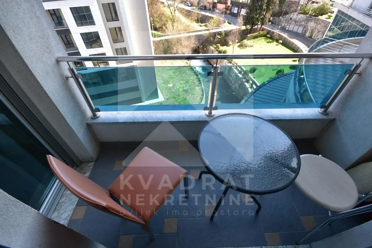 Small furnished balcony with a glass table and chairs and a view of the surroundings.