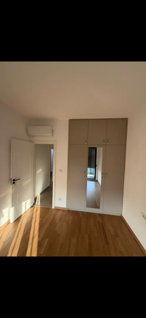 Bright bedroom with a fitted wardrobe, wooden flooring, and an air conditioner.