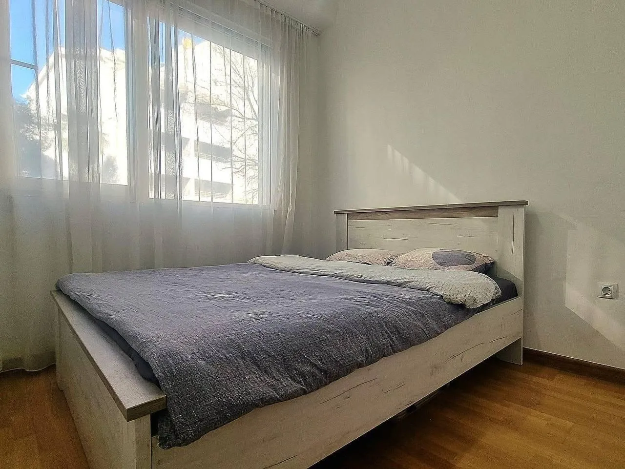 Svjetla spavaća soba sa bračnim krevetom i prozorom prekrivenim zavjesama.