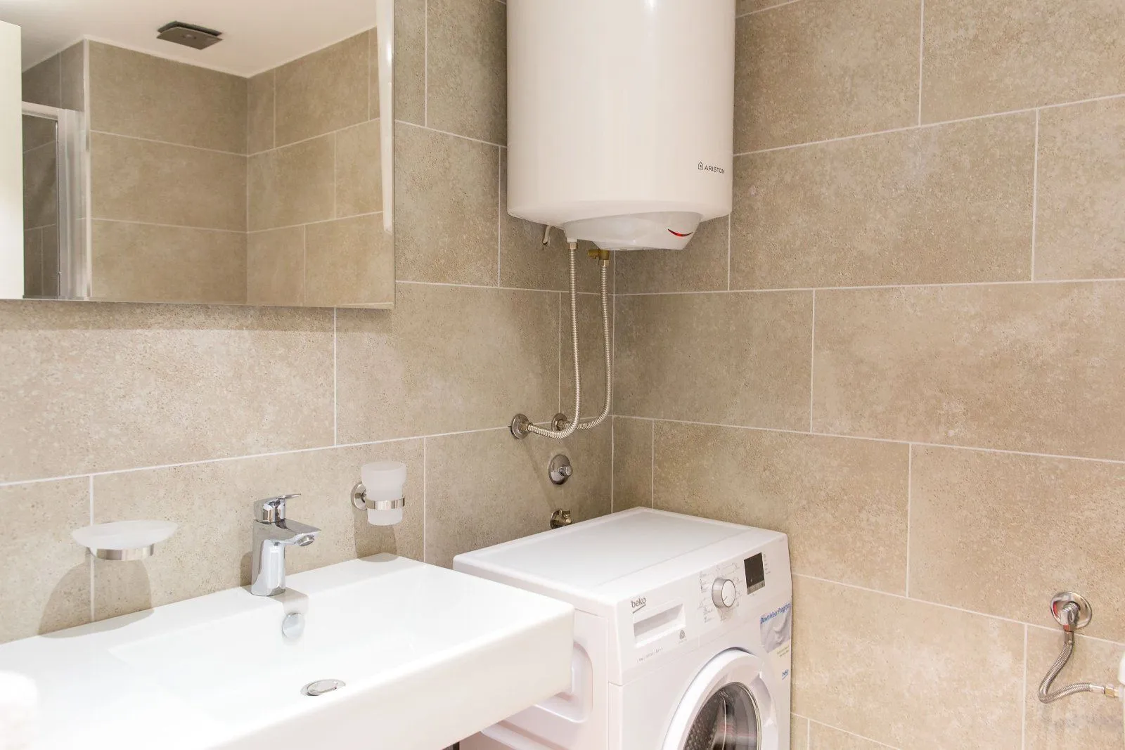 Bathroom with a sink, water heater, and washing machine tiled in beige.