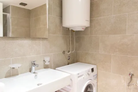 Bathroom with a sink, water heater, and washing machine tiled in beige. - image 5