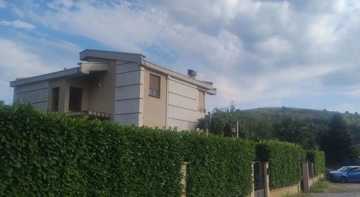 Exterior view of the house with a fenced yard surrounded by hedges.