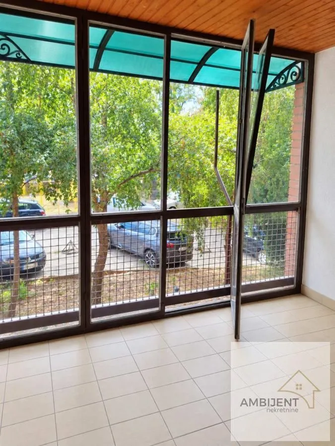 Zastakljeni balkon sa velikim prozorima i pogledom na zelenilo.