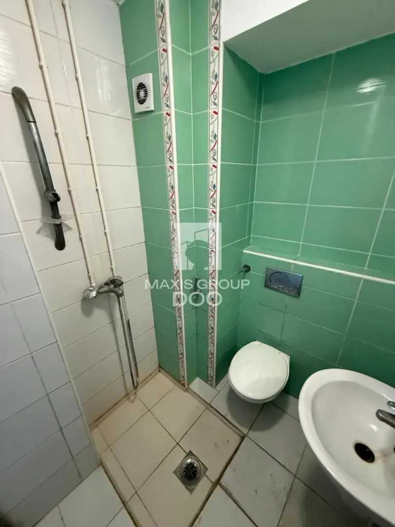 Smaller bathroom with a shower area, toilet bowl, and sink lined with ceramic tiles.