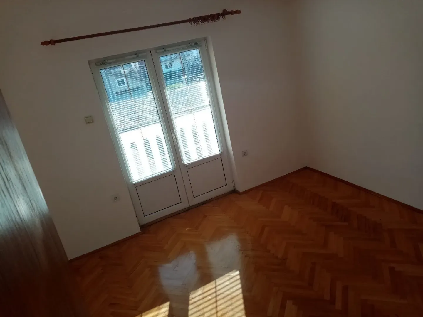 Empty room with parquet flooring and balcony doors.
