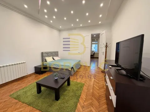Nameštena spavaća soba sa bračnim krevetom, TV komodom i parketom na podu. - image 4
